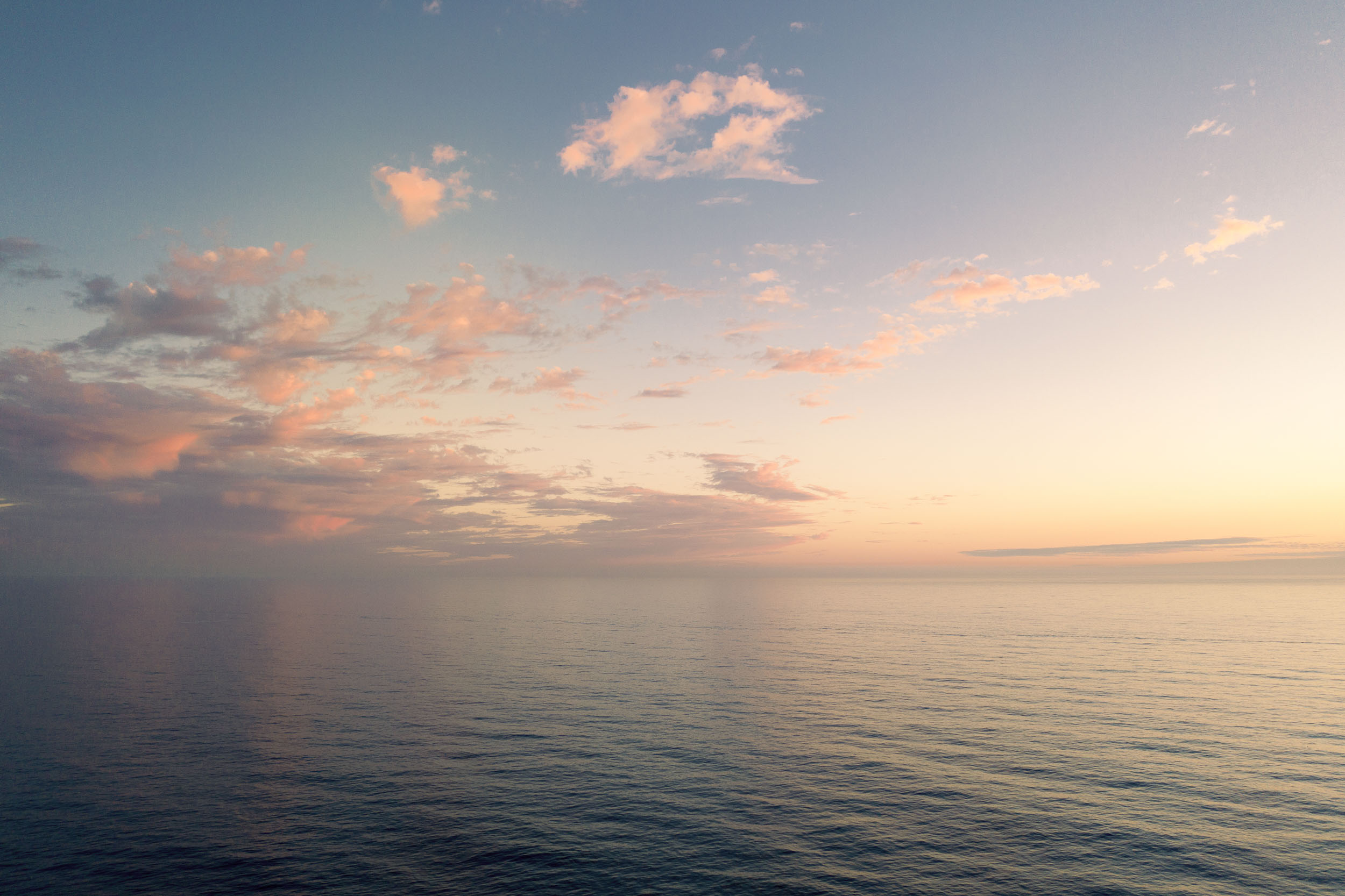 Dusk over the ocean with pink clouds in a deep blue sky