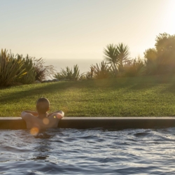 Young man relaxing in pool looking at the ocean at sunset