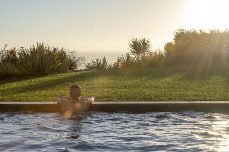 Young man relaxing in pool looking at the ocean at sunset