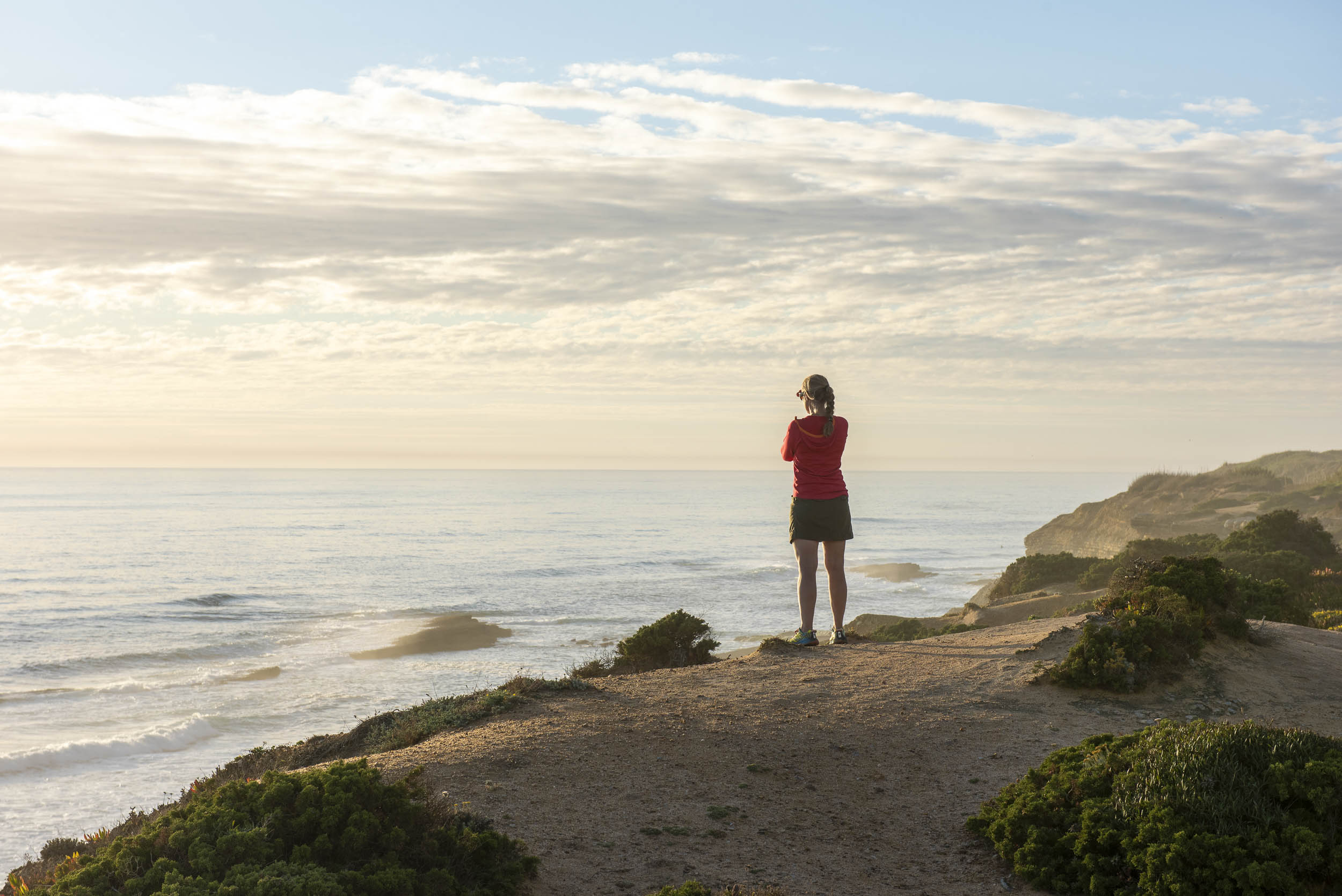 Woman watching the waves break from the cliffside above Ribeira D'Ilhas